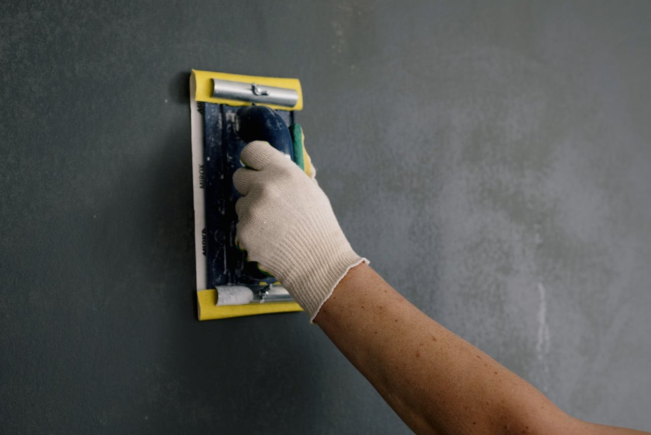 services-04 Close-up of a hand smoothing a wall with a spackle tool during home renovation.